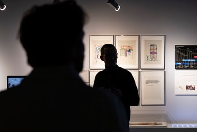 Silhouette von Personen vor beleuchteten Kunstwerken an der Wand.