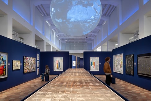 Kunstausstellung mit Gemälden in blauem Raum, grosse Kugel an der Decke.