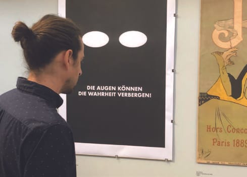Mann betrachtet Poster mit deutscher Aufschrift auf einer Ausstellung.