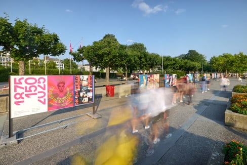 Verschwommene Menschen vor bunten Plakaten im Freien.