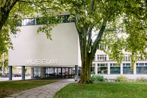 Aussenansicht eines modernen Gebäudes mit Museumsschild und Bäumen.