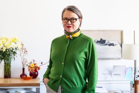 Frau in grünem Pullover im Wohnzimmer stehend.