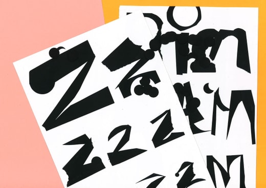 Abstrakte schwarze Buchstaben auf weissem Papier vor rosa Hintergrund.