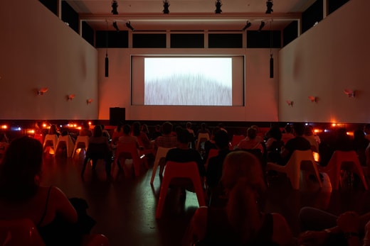 Menschen sehen in einem dunklen Raum einen Film auf einer Leinwand an.