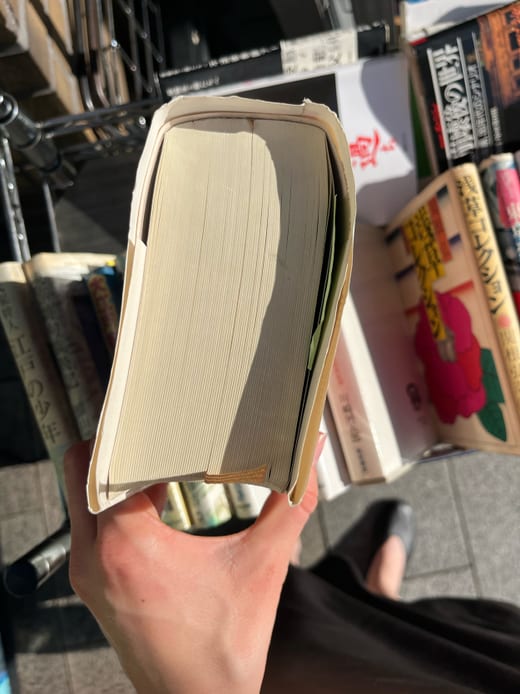 Hand hält ein geöffnetes Buch über einem Tisch mit Büchern.
