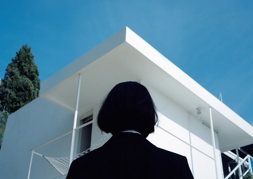 Person steht vor modernem, weissem Gebäude mit blauem Himmel.