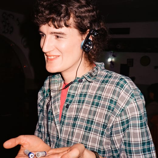 Person mit Kopfhörern lächelnd im karierten Hemd, hält etwas in den Händen.