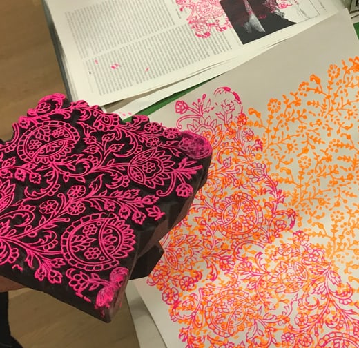 Holzblock mit floralem Muster neben bedrucktem Papier in Pink und Orange.",