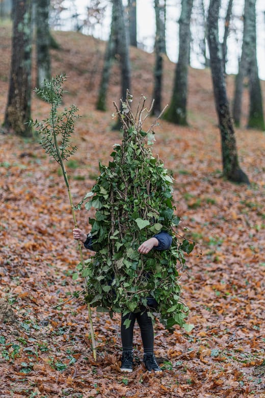 Person im Blätterkostüm in bewaldetem Gebiet.