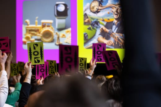 Menschen halten Schilder hoch bei einer Präsentation mit bunten Bildern im Hintergrund.