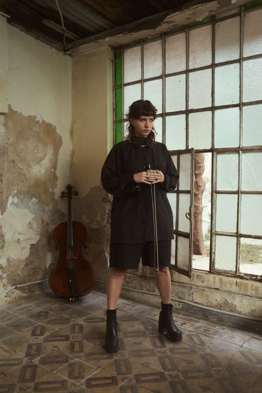 Person in schwarzer Kleidung in einem alten Raum mit Cello und grossen Fenstern.