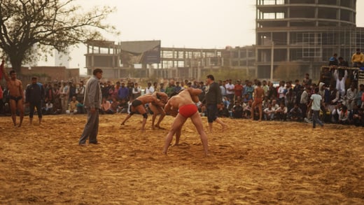 Zwei Ringer auf Sandplatz von Zuschauern umgeben.