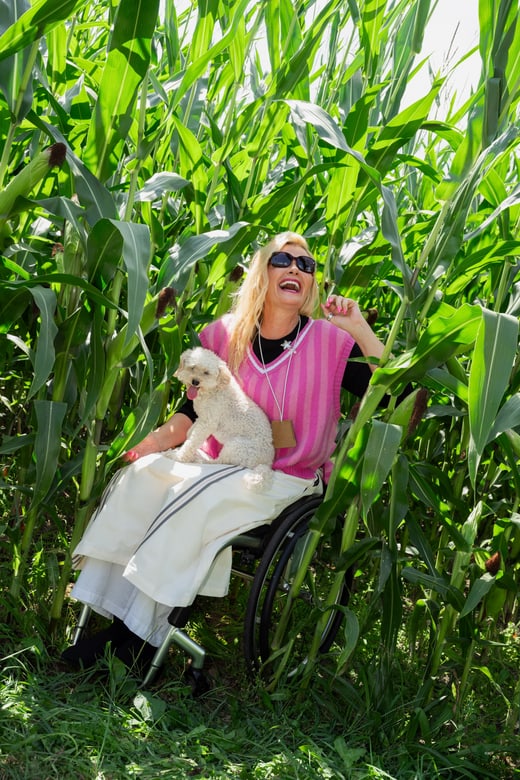 Frau im Rollstuhl mit Hund im Maisfeld lachend.