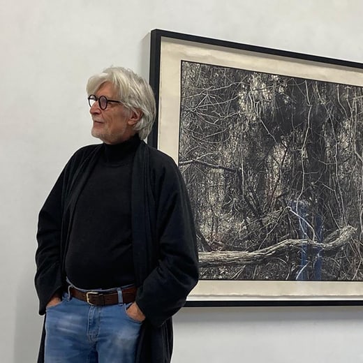 Georges Wenger in schwarzer Kleidung vor einem Kunstwerk an der Wand.
