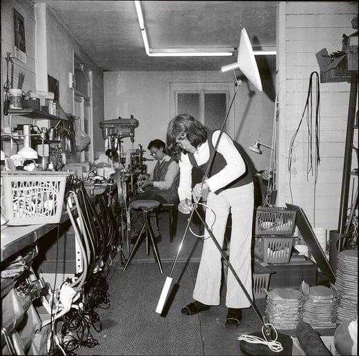 Person in Werkstatt, arbeitet an Lampe mit Werkzeugen im Hintergrund.