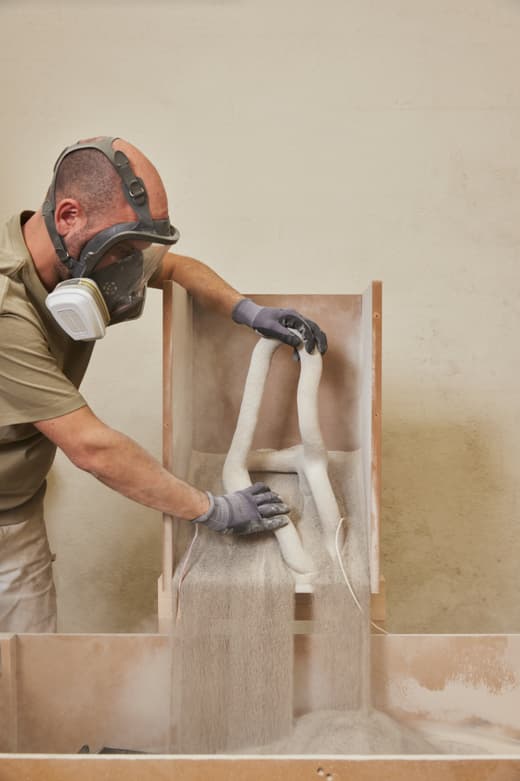 Person mit Maske arbeitet an einem Sandguss-Prozess.