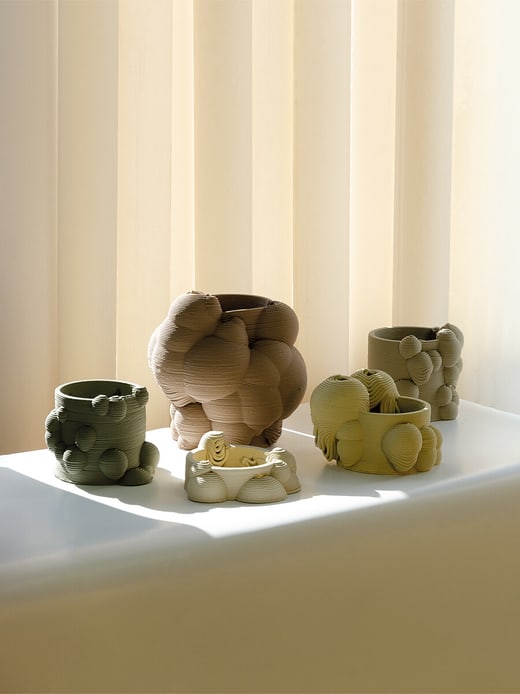 Mehrere organisch geformte Keramiktöpfe auf Fensterbank vor Jalousien.