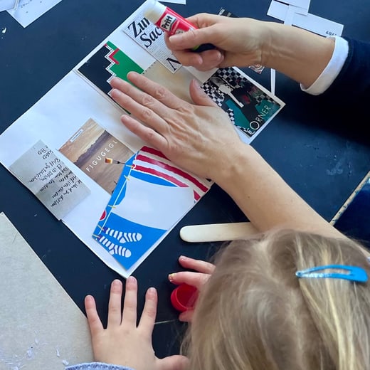 Kind bastelt Collage mit Hilfe eines Erwachsenen.