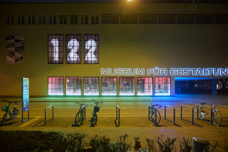Beleuchtetes Museum für Gestaltung mit Fahrrädern davor bei Nacht.